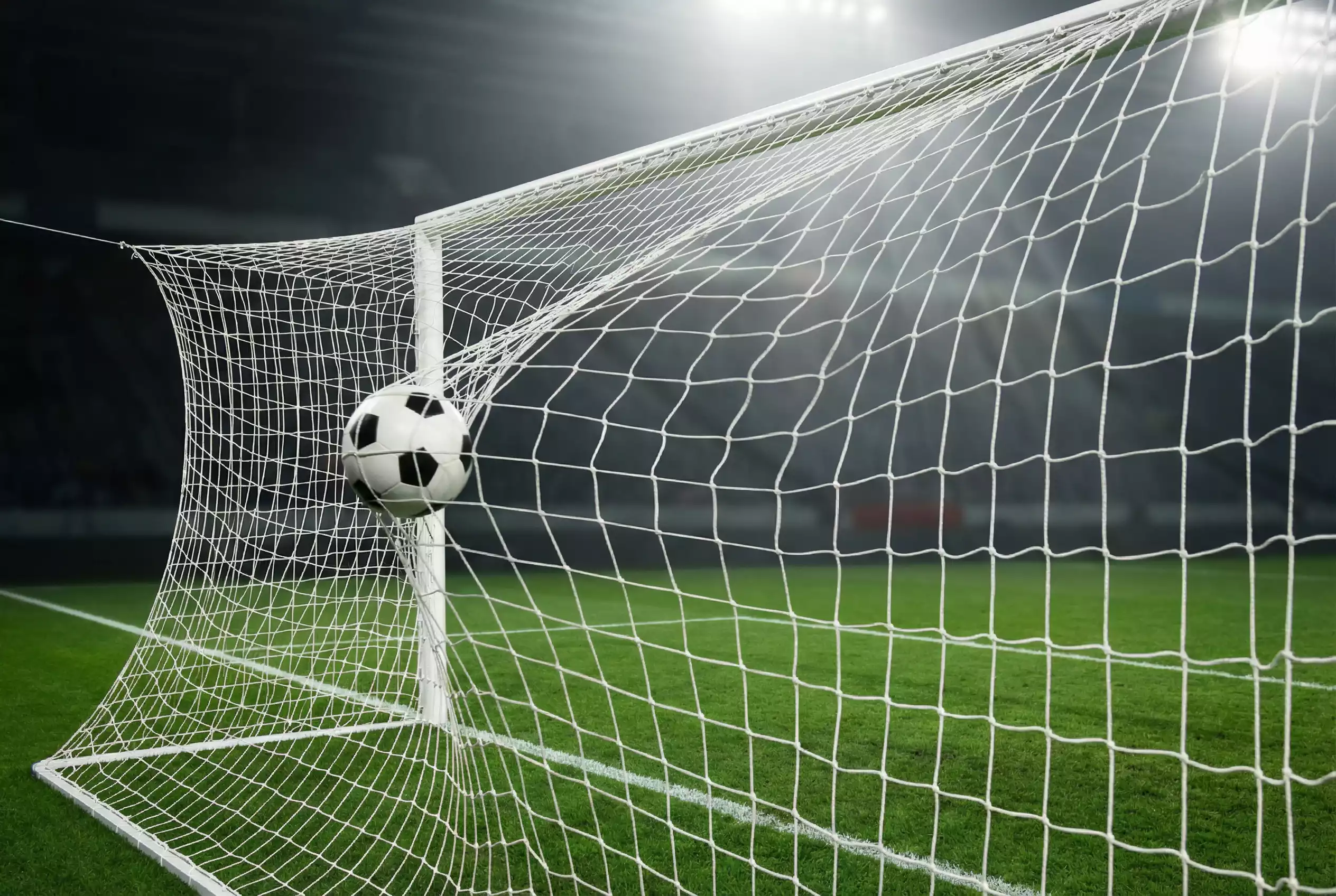 Red de portería de fútbol con un balón entrando en la escuadra bajo focos de estadio